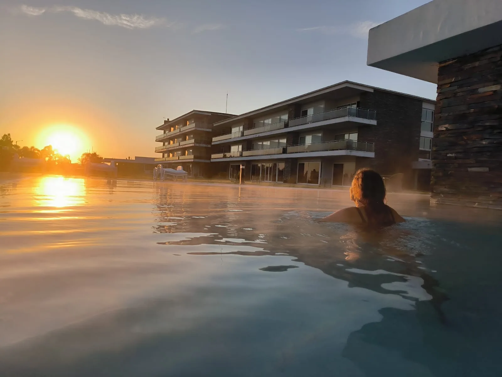The pool at Altos del Arapey at dusk, a woman in the water looking at the sunset