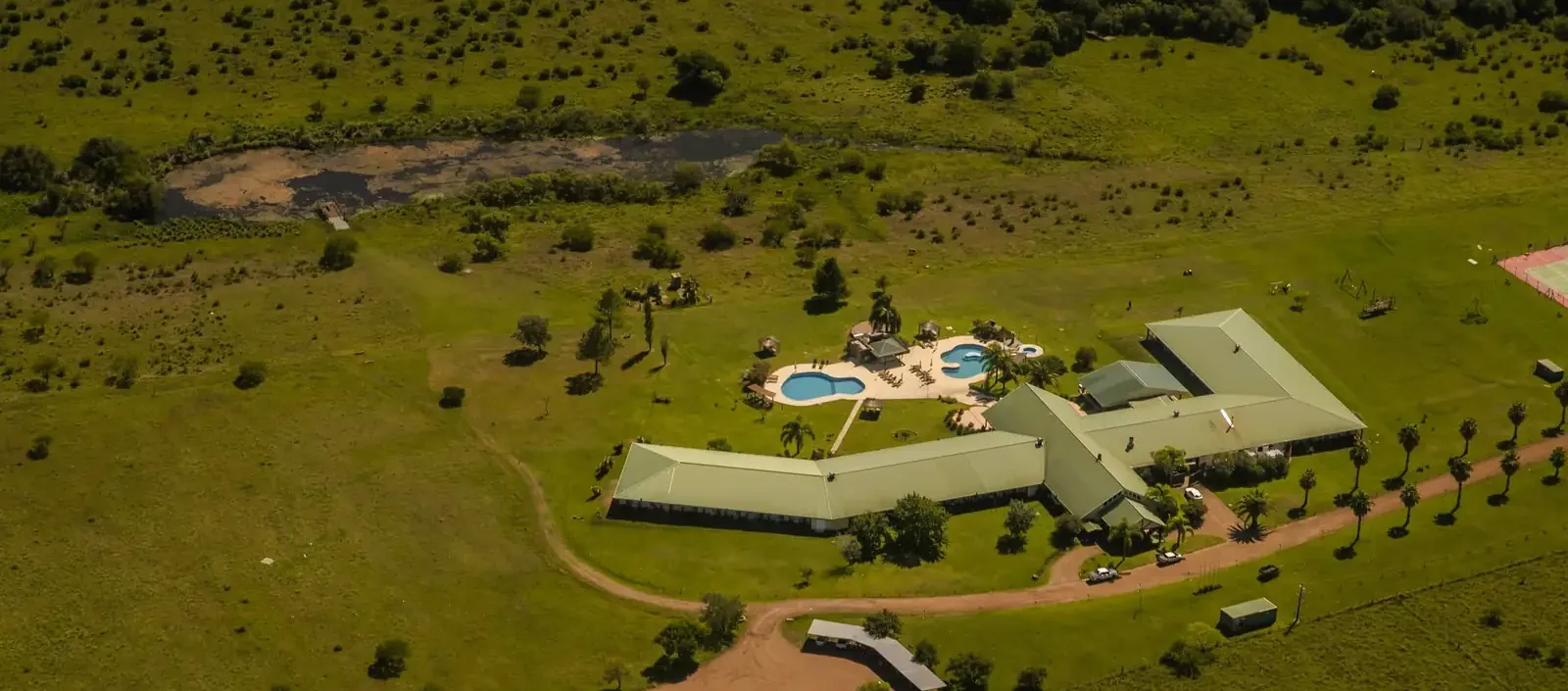 Hotel Los Naranjos from the air: the two low wings, the pools and the palm-lined drive, with the pond beyond