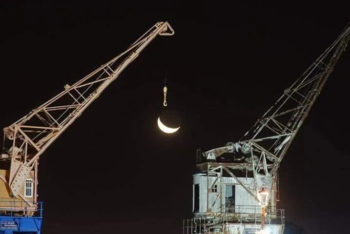 A crescent moon between the old port cranes of Salto, photographed by Marcelo Cattani