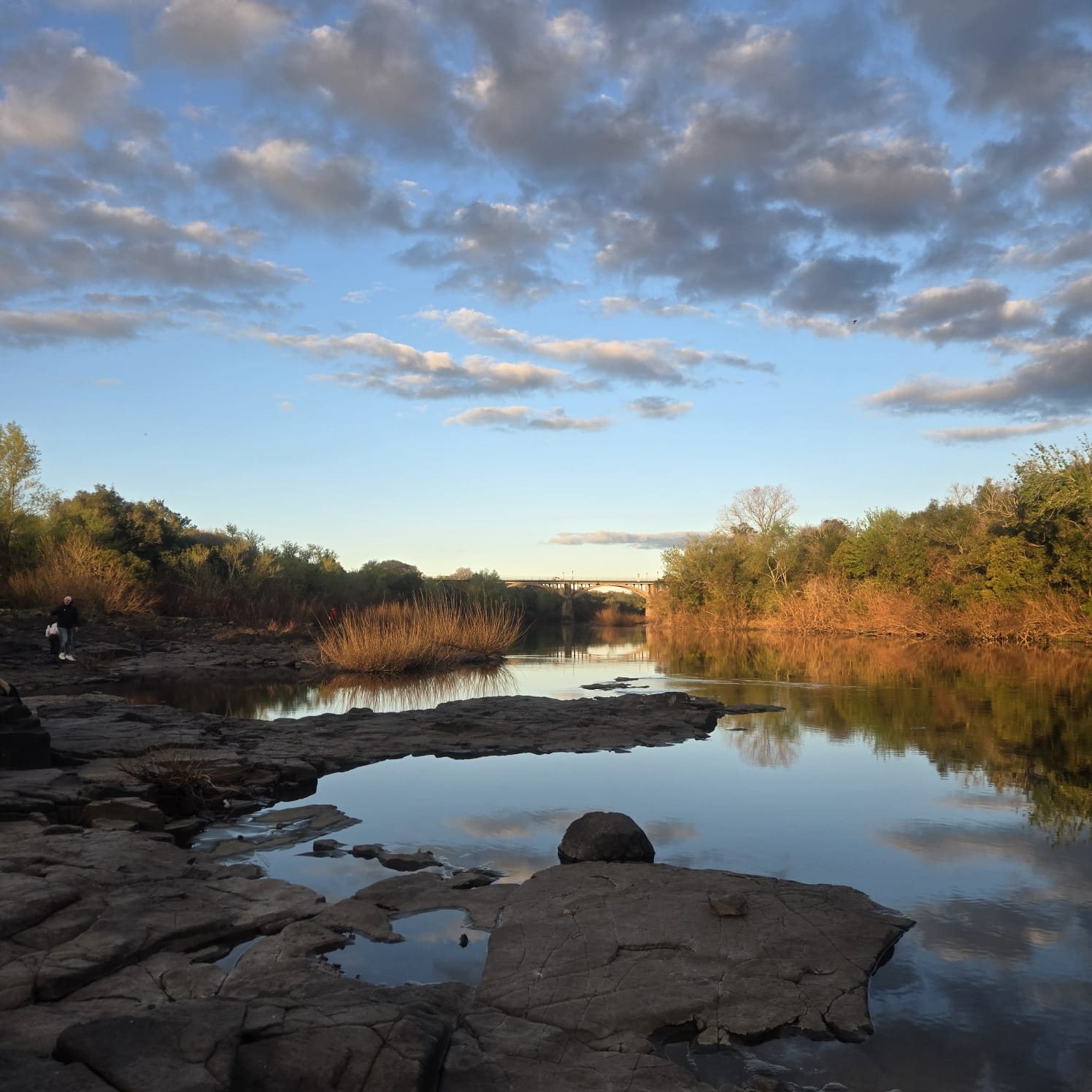 Rock pools on the sandstone shelf of the Río Daymán with the bridge at Termas del Daymán, Salto, Uruguay