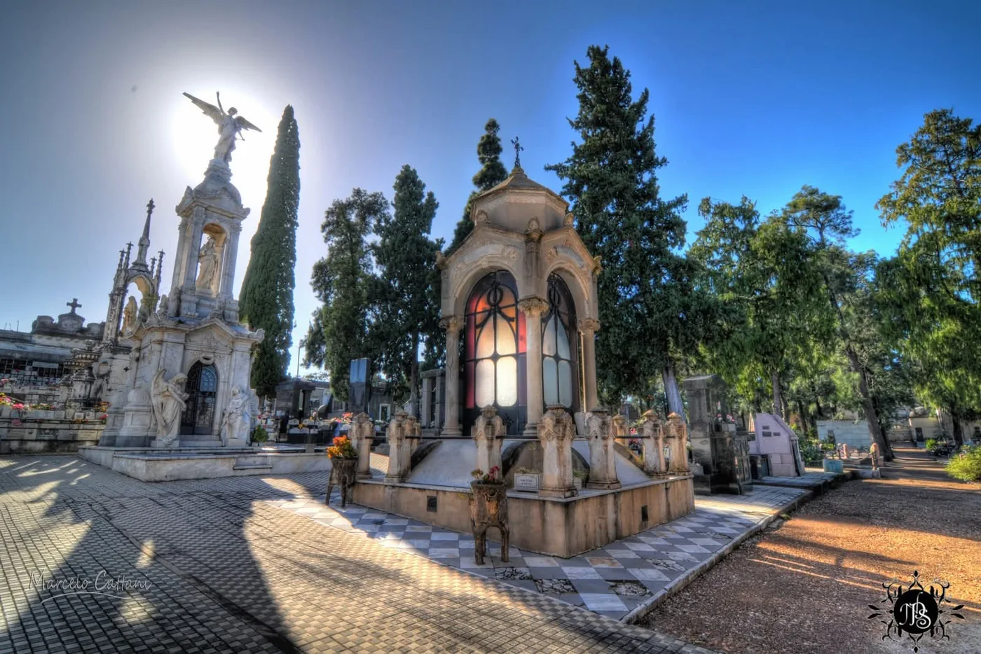 An angel-topped marble monument against the sun, a small chapel with stained glass and cypresses in the Central Cemetery of Salto