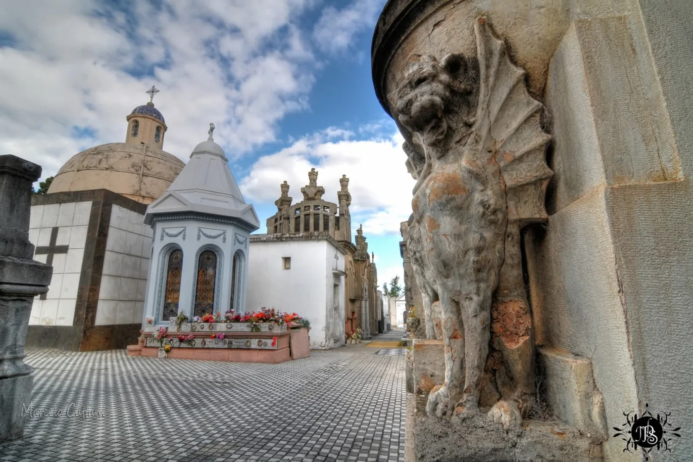 A stone gargoyle on a mausoleum, a pale-blue pavilion with stained glass and the chapel dome behind, Central Cemetery of Salto